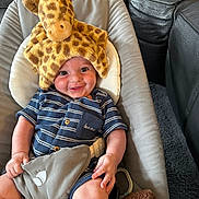 Jordan is registered to the contest to win money with this photo: baby, giraffe_hat, striped_clothing, smile, cushion, baby_seat, stuffed_toy, happy, child, indoor, cute, infant, portrait, comfort, playful, blue, soft_toy, seat_belt, relaxed, cheerful