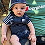 Jordan joined the competition — help win amazing prizes! baby, child, cap, striped_shirt, overalls, socks, adult, green_shirt, logo, outdoor, sunlight, bench, wood, hand, face, eyes, curious, sitting, casual, portrait
