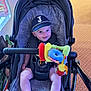 baby, stroller, cap, toy, plush_toy, smile, infant, child, cushion, clothing, sock, seatbelt, indoor, carpet, pattern, hand, face, person, cute, happy