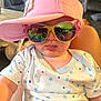 Jordan is registered to the contest to win money with this photo: baby, child, pink_cap, sunglasses, tongue_out, onesie, stars_pattern, indoor, reflection, person_reflection, cute, playful, close_up, infant, headwear, glasses, colorful, smiling, comfort, living_room