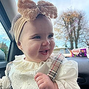 Adalyn is registered to the contest to win money with this photo: baby, child, headband, flower, smile, laughing, car_interior, window, clothing, plaid, white_blouse, cute, face, eyes, hand, autumn, trees, daylight, person, portrait