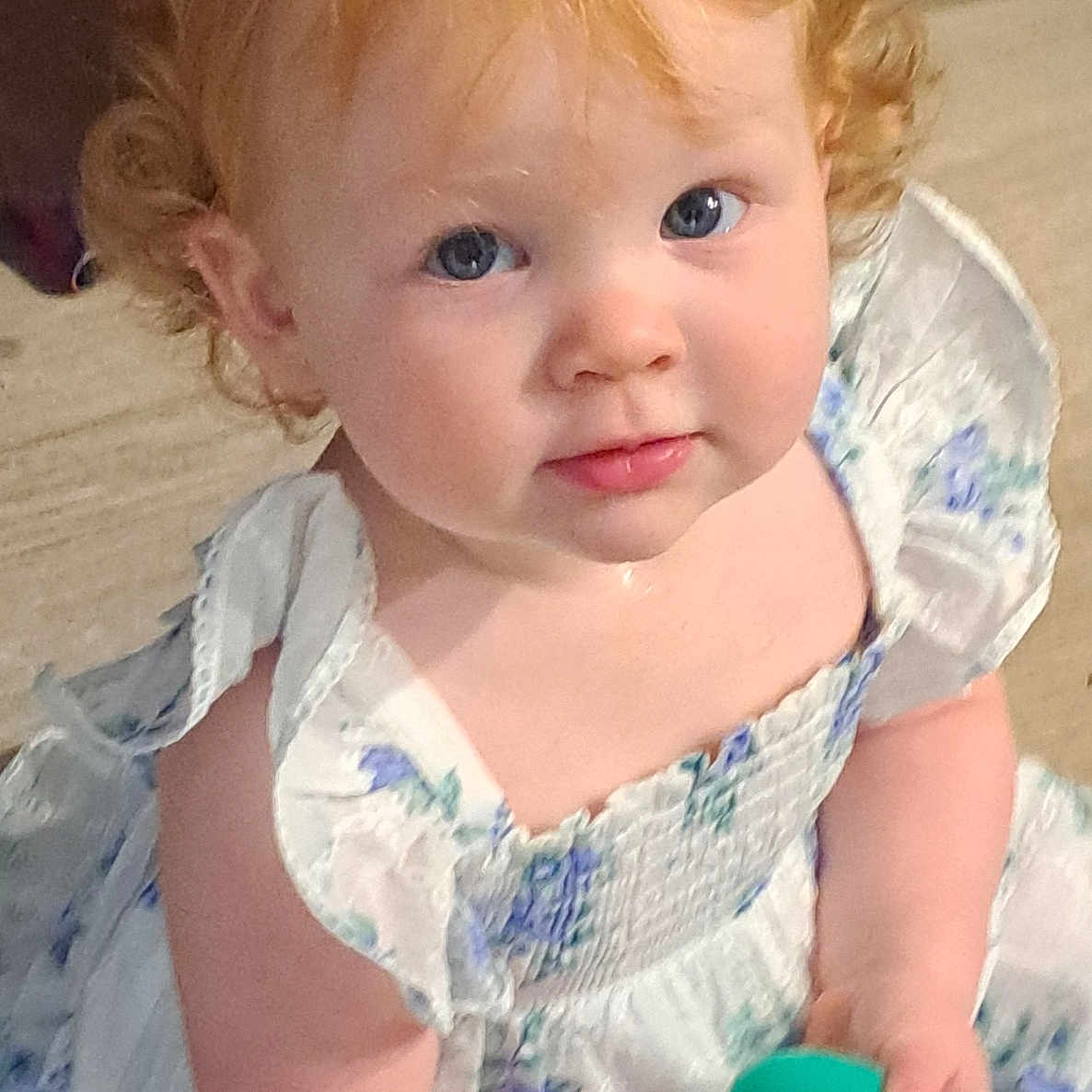 Amalie joined the competition — help win amazing prizes! child, toddler, curly_hair, blue_eyes, white_dress, floral_pattern, toy, indoor, portrait, cute, innocent, baby, person, holding, looking_up, rosy_cheeks, soft_lighting, small_hands, playful, curious