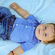 Yovani is registered to the contest to win money with this photo: baby, child, infant, blue_shirt, denim_jeans, blanket, outdoor, grass, smiling, portrait, cute, happy, lying_down, young_child, casual_clothing, soft_texture, skin, face, person, relaxed