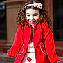 child, girl, red_coat, curly_hair, flower_headband, smiling, apple_pattern, skirt, outdoor, portrait, happy, cute, fashion, winter_clothing, playful, urban, young, person, standing, daylight