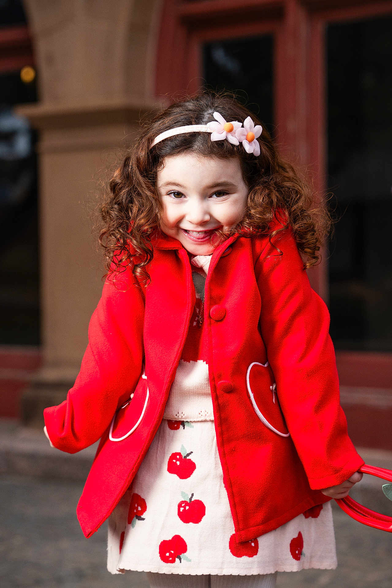 Mathilda joined the competition — help win amazing prizes! child, girl, red_coat, curly_hair, flower_headband, smiling, apple_pattern, skirt, outdoor, portrait, happy, cute, fashion, winter_clothing, playful, urban, young, person, standing, daylight