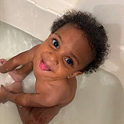 Legend is registered to the contest to win money with this photo: toddler, child, bath, water, curly_hair, tongue_out, playful, smiling, skin, sitting, bathtub, cute, happy, indoors, person, young_child, fun, bath_time, expression, splash