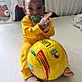 toddler, child, baby, pacifier, yellow_clothing, soccer_ball, sports, indoor, bed, footwearless, clapping, curly_hair, smiling, cute, playful, person, toy, bright_colors, home, young_child