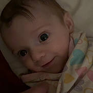 Autumn Olivia joined the competition — help win amazing prizes! baby, infant, smile, face, blanket, hand, wrapped, close_up, cute, child, person, bed, soft_lighting, indoors, cozy, pattern, heart, fabric, warm, tender