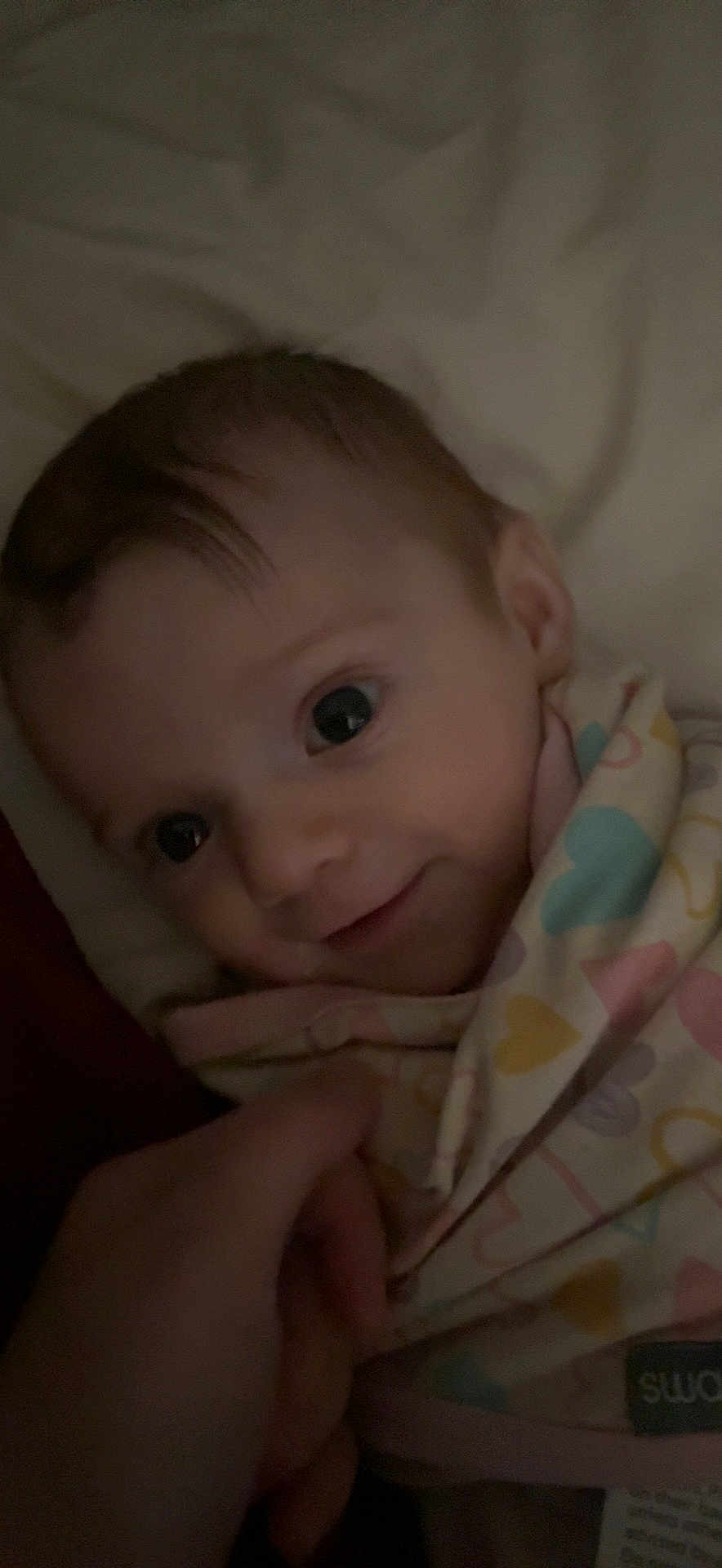 Autumn Olivia joined the competition — help win amazing prizes! baby, infant, smile, face, blanket, hand, wrapped, close_up, cute, child, person, bed, soft_lighting, indoors, cozy, pattern, heart, fabric, warm, tender