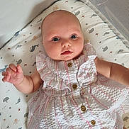 Elsie is registered to the contest to win money with this photo: baby, infant, dress, patterned_bedding, cushion, cute, chubby_cheeks, buttoned_dress, lying_down, indoors, child, person, face, hand, pink_stripes, white_dress, curious_expression, soft_lighting, mesh_side, baby_girl