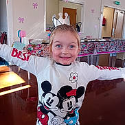 Phoebe joined the competition — help win amazing prizes! child, girl, smiling, crown_headband, mickey_mouse, minnie_mouse, sweatshirt, arms_outstretched, indoor, party, decorations, table, chairs, wall_bows, happy, blue_eyes, light, floor, clothing, celebration
