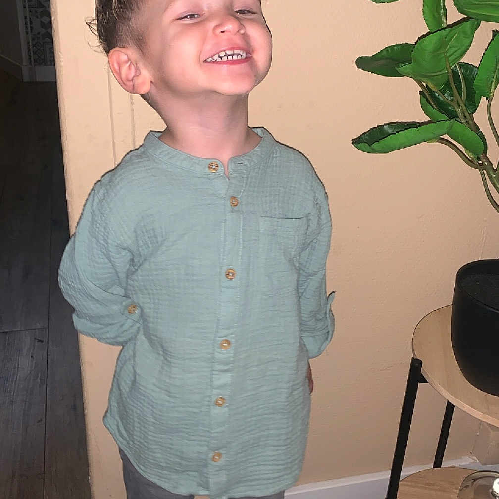 Lyzandro a rejoint le concours — aidez-le/la à gagner de superbes lots ! boy, casual_clothing, child, curly_hair, floor, furniture, gray_pants, green_shirt, happy, home, indoor, jar, plant, portrait, smiling, standing, wall, white_sneakers, wooden_floor, wooden_table