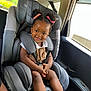 child, toddler, car_seat, smile, hair_buns, pink_ribbons, clothing, shoes, car_interior, seatbelt, happy, person, portrait, baby, cute, sitting, safety, window, daylight, vehicle