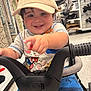toddler, child, cap, smile, pointing, shopping_cart, store, clothing, shorts, toy, happy, face, person, indoor, retail, footwear, pants, handlebar, cute, boy