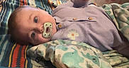 River joined the competition — help win amazing prizes! baby, blanket, carpet, chair, child, clothing, colorful, cozy, curious, door, floor, furniture, home, indoor, lying_down, office_chair, pacifier, pattern, person, room