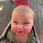 River is registered to the contest to win money with this photo: baby, blond_hair, bright_eyes, carrier, casual, child, curious, cute, daylight, face, green_clothing, hand, infant, outdoor, person, portrait, rosy_cheeks, small_hands, smiling, wooden_floor