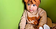 Kehlani is registered to the contest to win money with this photo: baby, child, headband, orange_bow, green_wall, plush_toy, pink_toy, cozy_clothing, socks, seated, curious, indoors, cute, wide_eyes, portrait, toddler, soft_texture, playful, infant, colorful