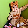 Kehlani is registered to the contest to win money with this photo: baby, child, smile, headband, orange_bow, blue_eyes, beige_outfit, textured_clothing, plush_toy, pink_toy, blanket, green_wall, sitting, happy, cute, indoor, portrait, cozy, infant, person