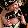 baby, infant, child, cow_print, hat, bonnet, clothing, black_and_white, pattern, cute, holding_hand, skin, person, newborn, portrait, indoors, background, fabric, relaxed, expression