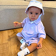 Ayden a rejoint le concours — aidez-le/la à gagner de superbes lots ! toddler, child, baby, sitting, floor, hat, bucket_hat, socks, white_socks, purple_outfit, shorts, shirt, indoor, wooden_floor, couch, furniture, curious, portrait, person, clothing