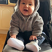 Maé participe au concours pour gagner de l'argent avec cette photo : baby, child, stroller, hoodie, smiling, indoor, white_shoes, cute, face, person, seated, clothing, happy, infant, furniture, black_stroller, toy, footwear, babywear, warm_clothing