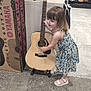 child, girl, guitar, musical_instrument, store, acoustic_guitar, footwear, carpet, floral_dress, smiling, indoor, display, shopping, toy, music_store, wood, sandals, young_child, person, happy