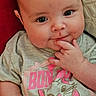 Ainsley is registered to the contest to win money with this photo: baby, infant, child, cute, smiling, gray_shirt, pink_shorts, cartoon_cat, hand, face, eyes, sitting, red_background, beige_background, skin, person, clothing, portrait, indoors, young