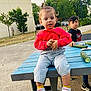 Mirela Marin participe au concours pour gagner de l'argent avec cette photo : boy, casual_clothing, child, concrete, cucumber, curious_expression, daylight, jeans, nature, outdoor, park, person, picnic_table, playing, red_sweater, sitting, sneakers, toddler, trees, yellow_socks