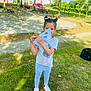 casual_clothing, child, daylight, fun, grass, greenery, nature, outdoor, paper_fan, park, person, playful, recreation, shadow, shoes, smile, sneakers, sunlight, trees, young