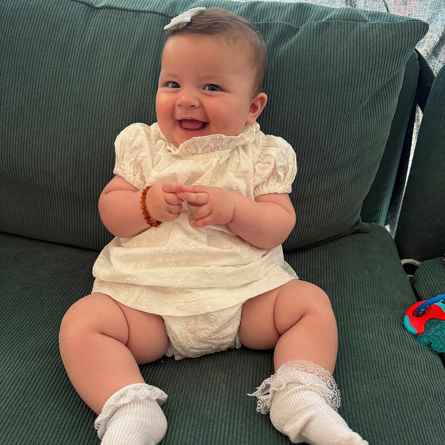 Zara is registered to the contest to win money with this photo: baby, bow, bracelet, child, chubby_legs, couch, cute, green_couch, happy, head_accessory, indoor, infant, person, plush, portrait, sitting, smiling, socks, toy, white_dress