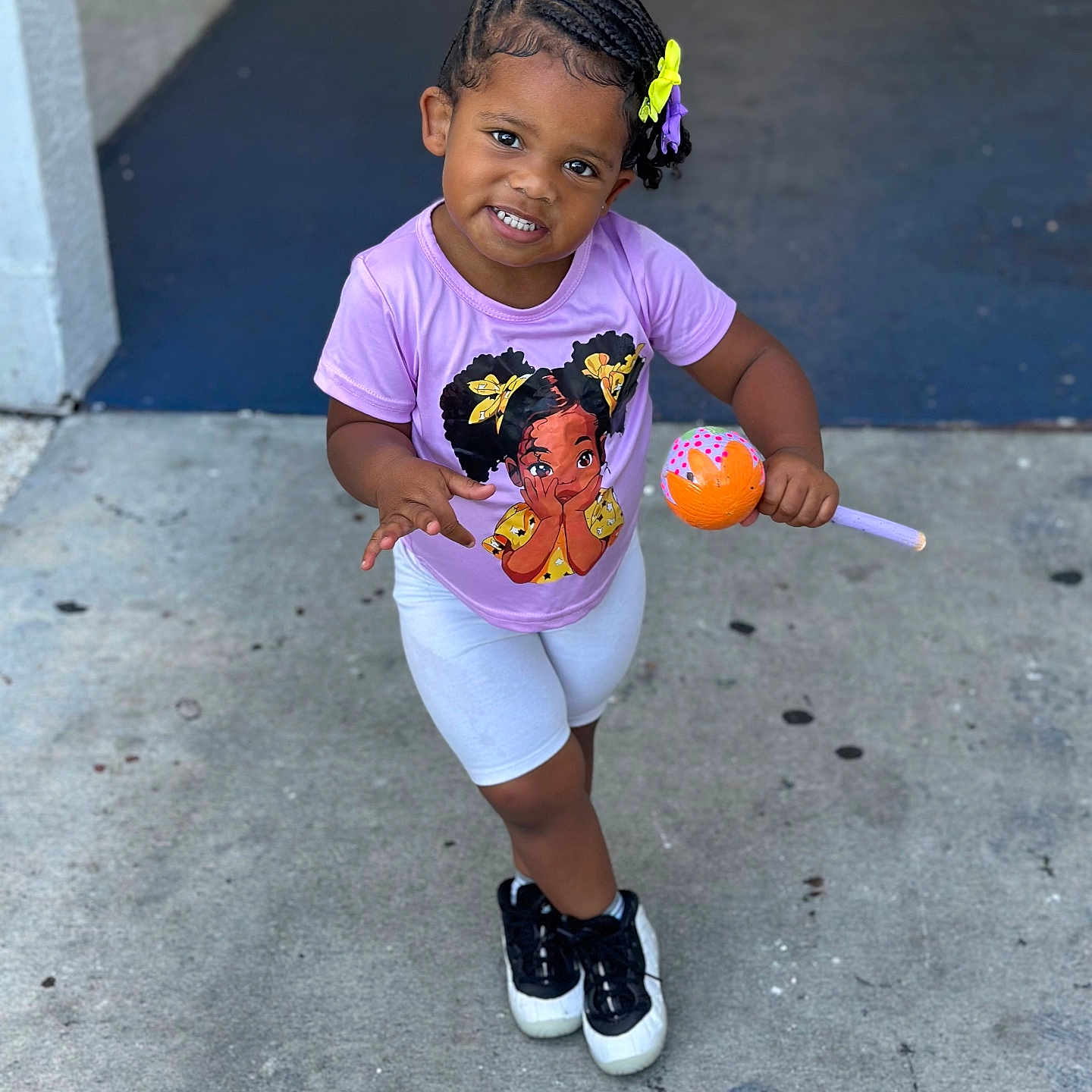 Kailyn joined the competition — help win amazing prizes! black_shoes, braided_hair, cartoon_graphic, child, concrete, cute, hair_bow, happy, lollipop_toy, outdoor, person, playful, purple_tshirt, sidewalk, smiling, standing, toddler, toy, white_shorts, young_child