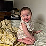 baby, bed, bib, blanket, child, cute, face, furniture, happy, home, indoor, infant, onesie, person, room, sitting, skin, smiling, television, young