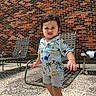 toddler, child, swimsuit, dinosaur_pattern, barefoot, outdoor, sunny, brick_wall, patio, concrete_floor, chair, metal_chair, shadow, expression, person, summer, cute, standing, playful, young_child