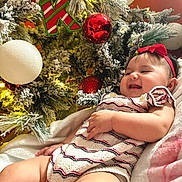 Kaylani joined the competition — help win amazing prizes! baby, infant, smiling, christmas_tree, ornament, red_bow, holiday, festive, knit_outfit, lights, decoration, happy, child, indoor, celebration, seasonal, cute, cozy, portrait, sitting