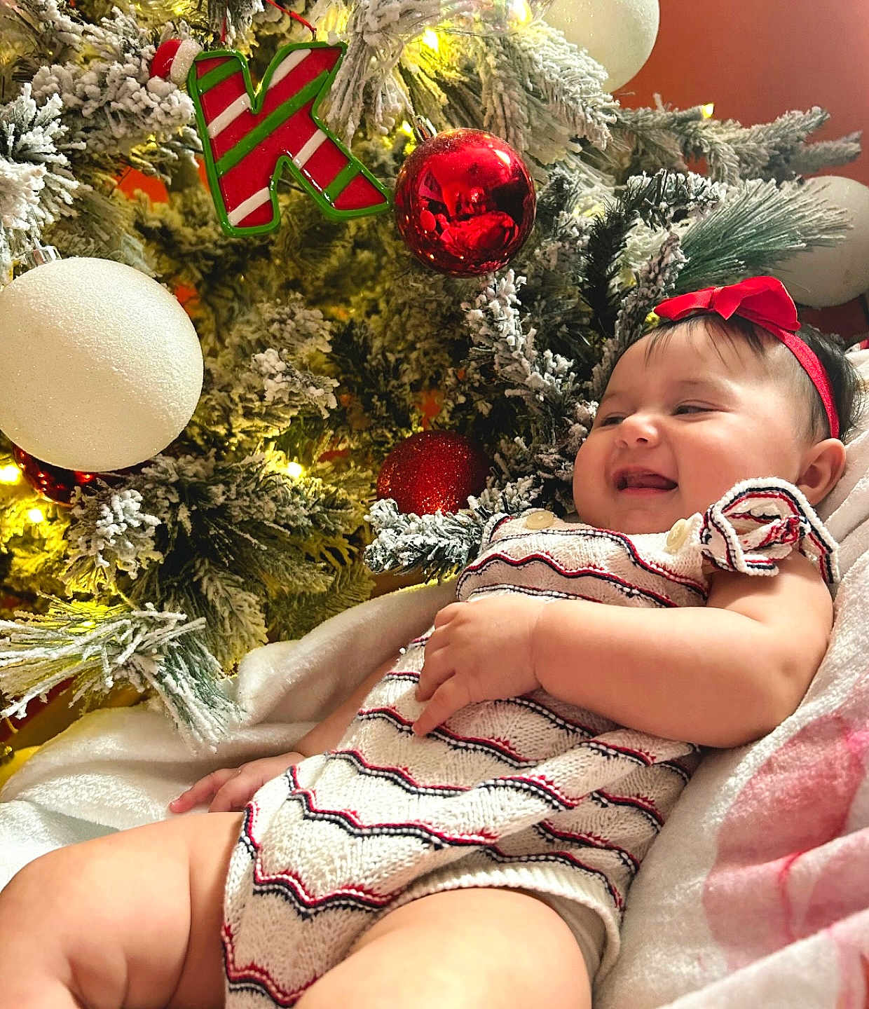 Kaylani joined the competition — help win amazing prizes! baby, infant, smiling, christmas_tree, ornament, red_bow, holiday, festive, knit_outfit, lights, decoration, happy, child, indoor, celebration, seasonal, cute, cozy, portrait, sitting