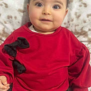 Selena is registered to the contest to win money with this photo: baby, black_bows, blanket, child, clothing, cozy, cute, eyelashes, face, hands, happy, head, indoor, infant, portrait, red_sweater, sitting, smile, soft_texture, young