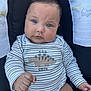 baby, child, infant, blue_eyes, striped_clothing, dinosaur_embroidery, onesie, car_seat, safety_warning, cute, chubby_cheeks, hand, portrait, indoors, seated, young_child, close_up, face, human, expression