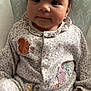 Bella joined the competition — help win amazing prizes! baby, infant, onesie, animal_patch, cute, child, face, smile, seated, cozy, patterned_clothing, indoor, portrait, young_child, cushion, soft_lighting, curious, hand, closeup, comfortable