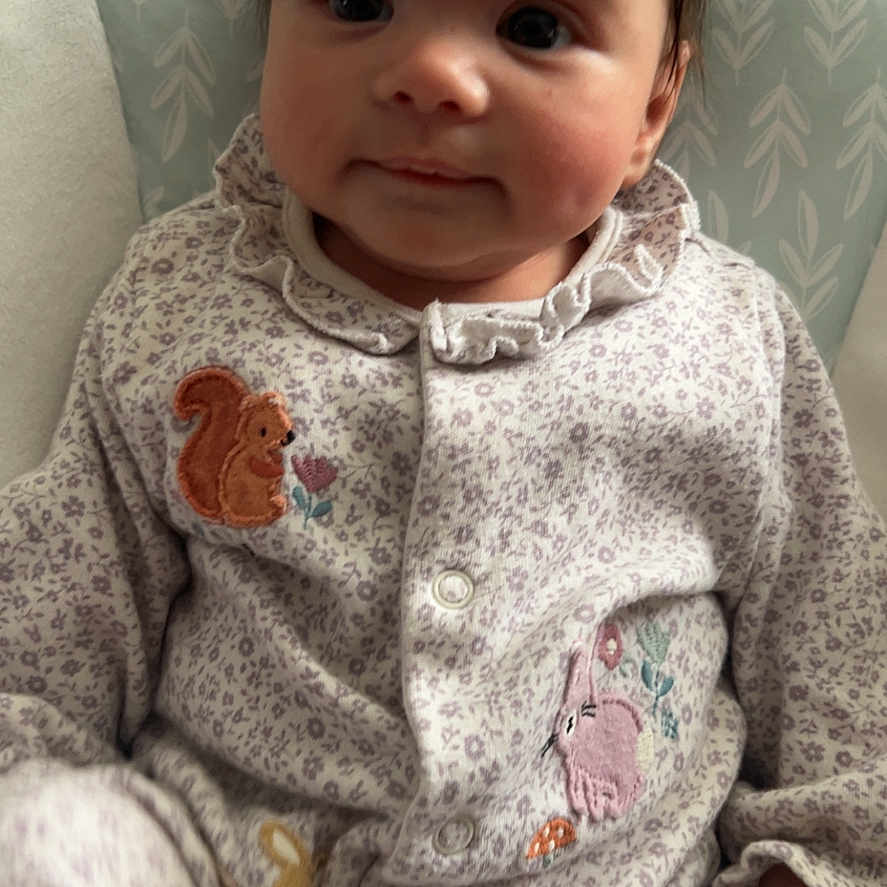 Bella joined the competition — help win amazing prizes! animal_patch, baby, child, closeup, comfortable, cozy, curious, cushion, cute, face, hand, indoor, infant, onesie, patterned_clothing, portrait, seated, smile, soft_lighting, young_child