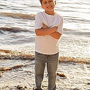 Andreas is registered to the contest to win money with this photo: child, boy, beach, sand, water, ocean, barefoot, casual_clothing, white_shirt, jeans, smiling, standing, sunlight, outdoor, nature, waves, happy, summer, portrait, daytime