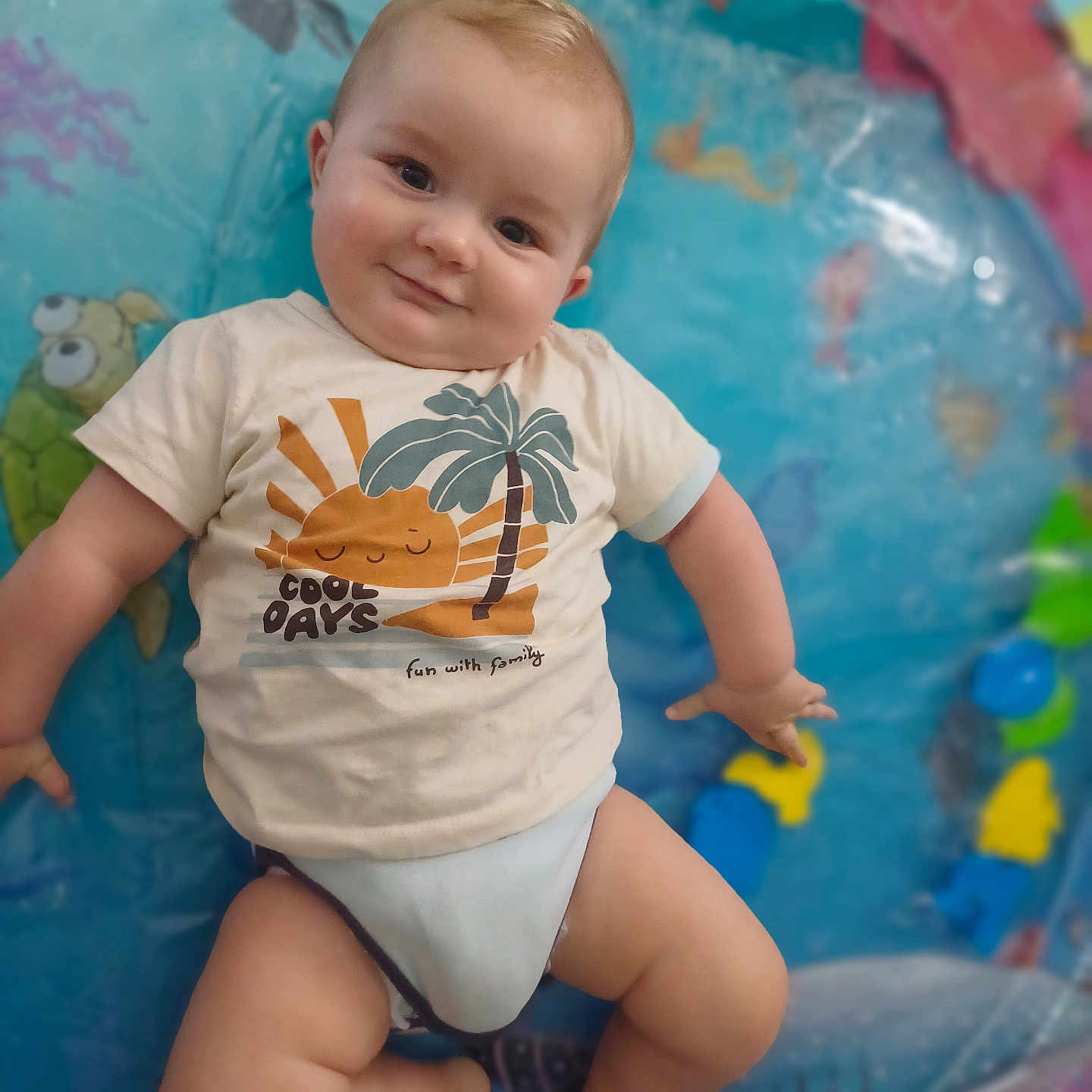 Léo a rejoint le concours — aidez-le/la à gagner de superbes lots ! baby, child, chubby_cheeks, colorful, cute, fish, happy, indoor, infant, inflatable_pool, legs, palm_tree, playful, relaxed, sea_creatures, skin, smile, sun_graphic, tshirt, turtle