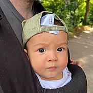 Alfie is registered to the contest to win money with this photo: baby, child, infant, cap, green_cap, baby_carrier, adult, beard, outdoor, forest, path, nature, portrait, closeup, face, curious, expression, skin, clothing, daylight