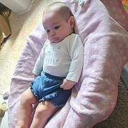 Irie is registered to the contest to win money with this photo: baby, infant, child, pink_blanket, blue_shorts, white_shirt, indoor, carpet, seat, cushion, relaxing, solemn, young_child, person, portrait, soft_texture, home, floor, casual_clothing, cute