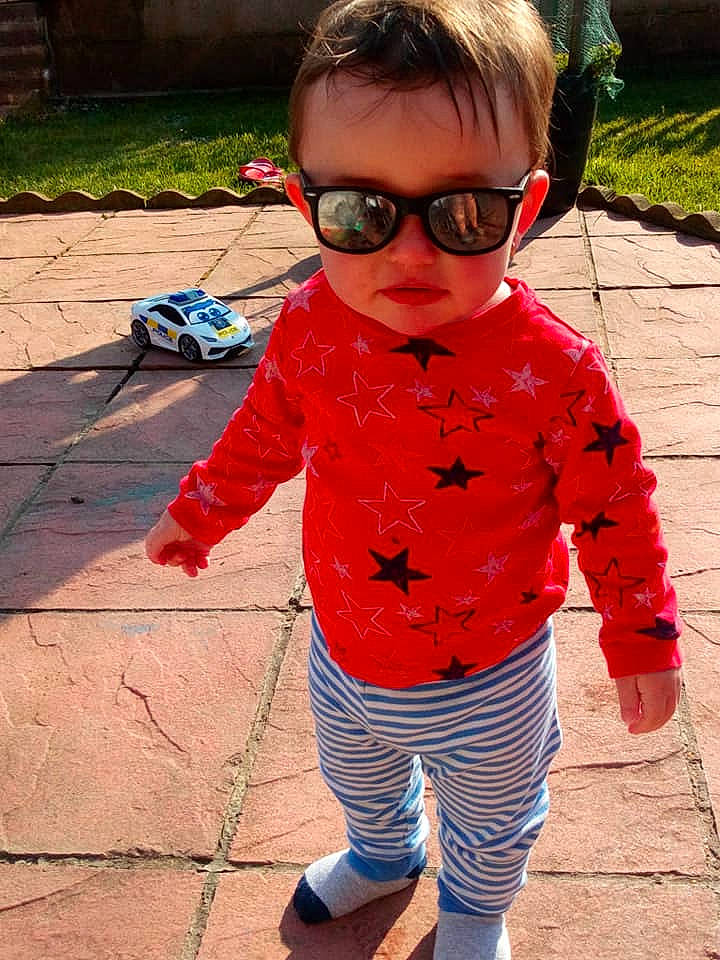 Noah is registered to the contest to win money with this photo: child, cool, eyewear, glasses, head, lip, outerwear, person, personal_protective_equipment, plant, play, sleeve, smile, sunglasses, t_shirt, toddler, vision_care