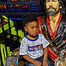 child, boy, pirate, statue, amusement_park, colorful, neon, indoor, reflection, phone, casual_clothing, blue_shoes, jeans, tshirt, seated, expression, playful_background, decor, portrait, young