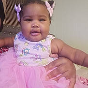 Armani is registered to the contest to win money with this photo: baby, child, tutu, pink, dress, bows, hair_accessory, smile, drool, hand, holding, indoor, wall, person, cute, infant, clothing, portrait, young_child, happy