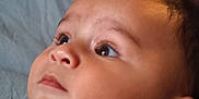 Idriss a rejoint le concours — aidez-le/la à gagner de superbes lots ! baby, close_up, face, infant, child, portrait, curious, gazing, lying_down, clothing, text_on_clothing, blue_shirt, soft_light, indoor, blanket, skin, hair, head, young_child, expression