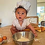 Idriss participe au concours pour gagner de l'argent avec cette photo : baby, child, chef_hat, flour, eggs, croissants, wooden_table, baking, surprised_expression, cooking, kitchen, rolling_pin, food, indoor, person, cute, messy_face, white_shirt, home, curly_hair