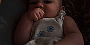 Paisley is registered to the contest to win money with this photo: baby, infant, thumb_sucking, blanket, bed, sleepy, dark, cozy, person, indoor, pattern, hand, face, adult, tattoo, sleeveless_shirt, resting, closeup, low_light, portrait