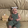 baby, infant, smiling, headband, green_overalls, couch, leather, wooden_sign, flower_shape, four_months, child, indoors, happy, drool, sitting, cute, young_child, portrait, people, one_person